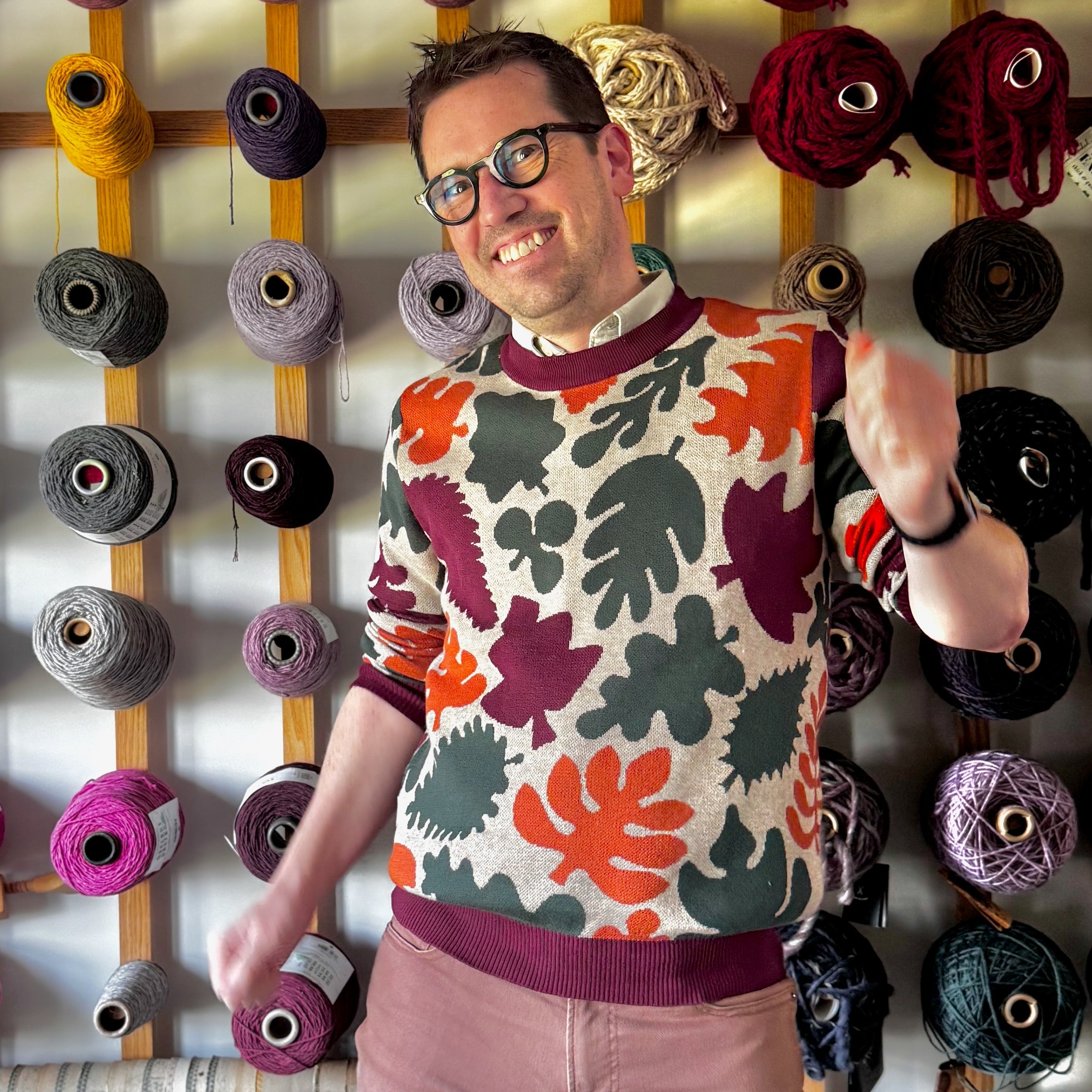Jedd standing wearing a tan sweater with a detailed pattern of colored leaves.