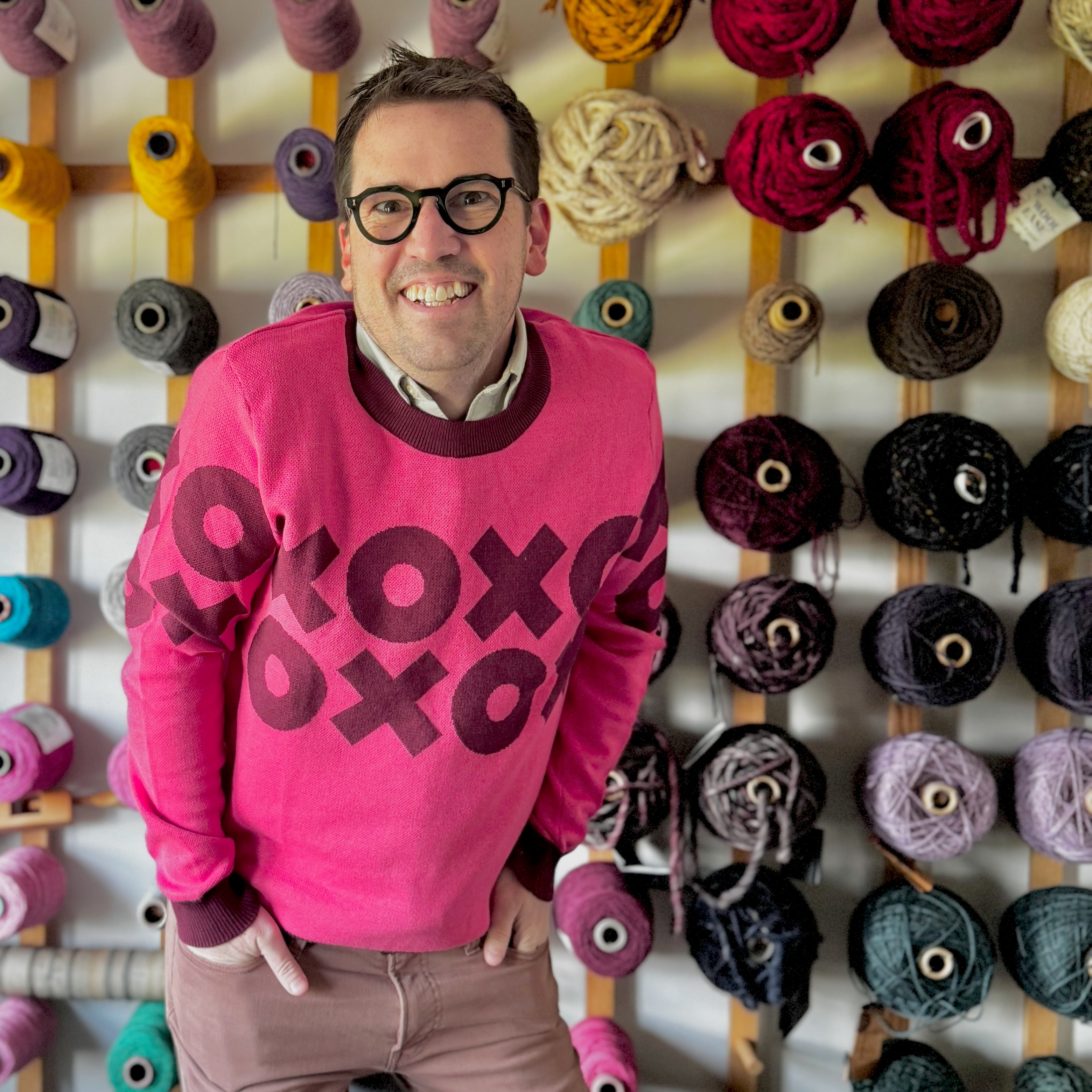 A portrait of Jedd wearing a pink sweater with an XOXO design