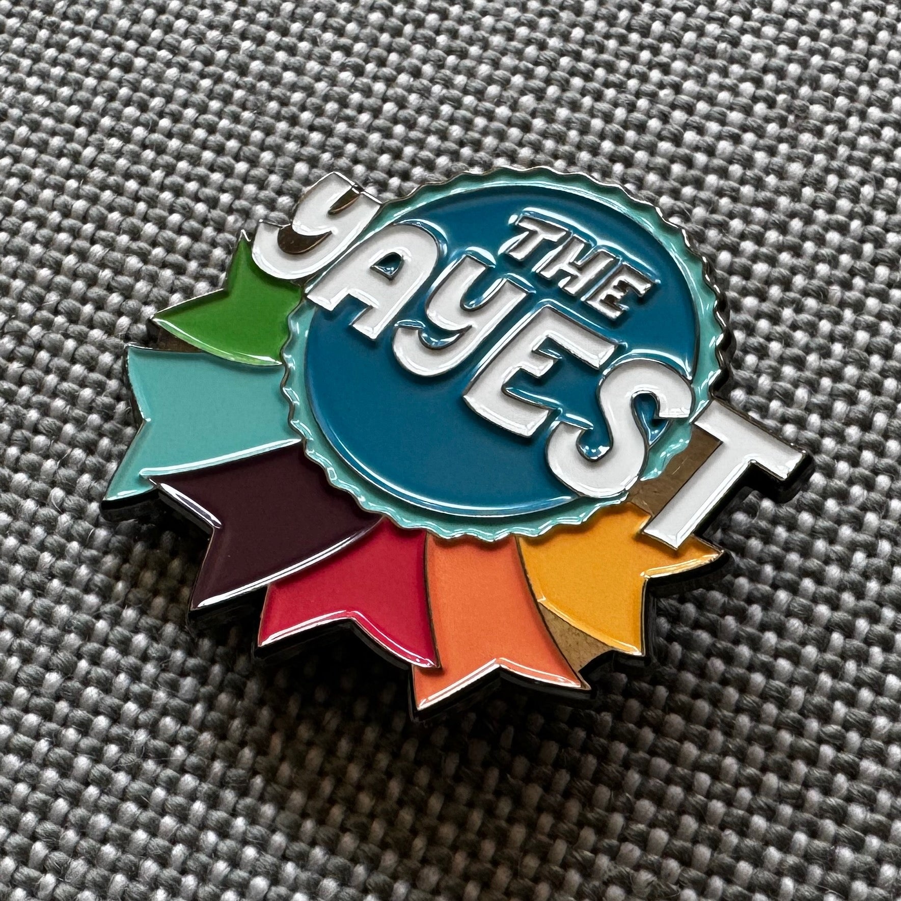 Enamel pin in a ribbon shape that reads "The Yayest"