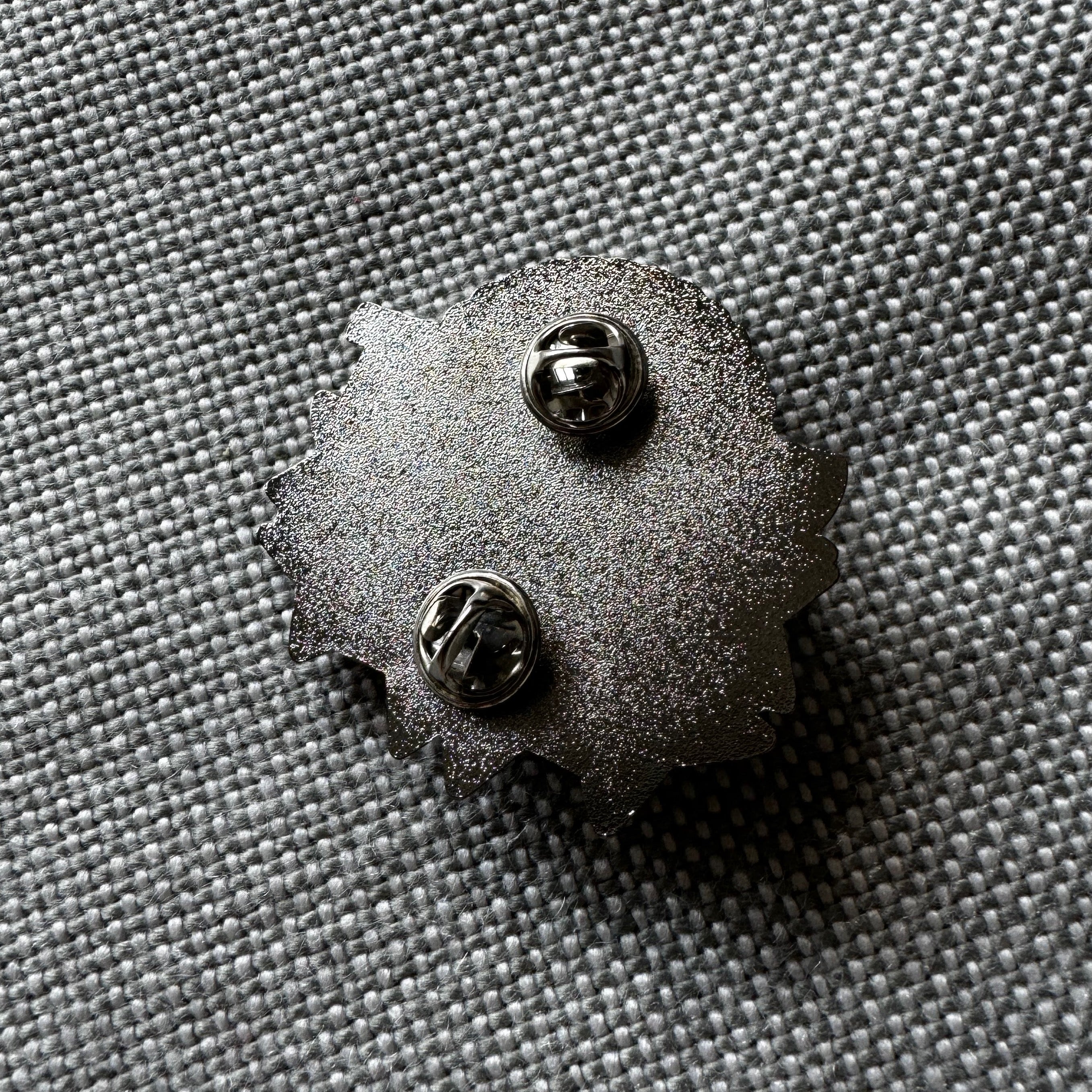 Detail of the back of an enamel pin with two pins and butterfly closures.
