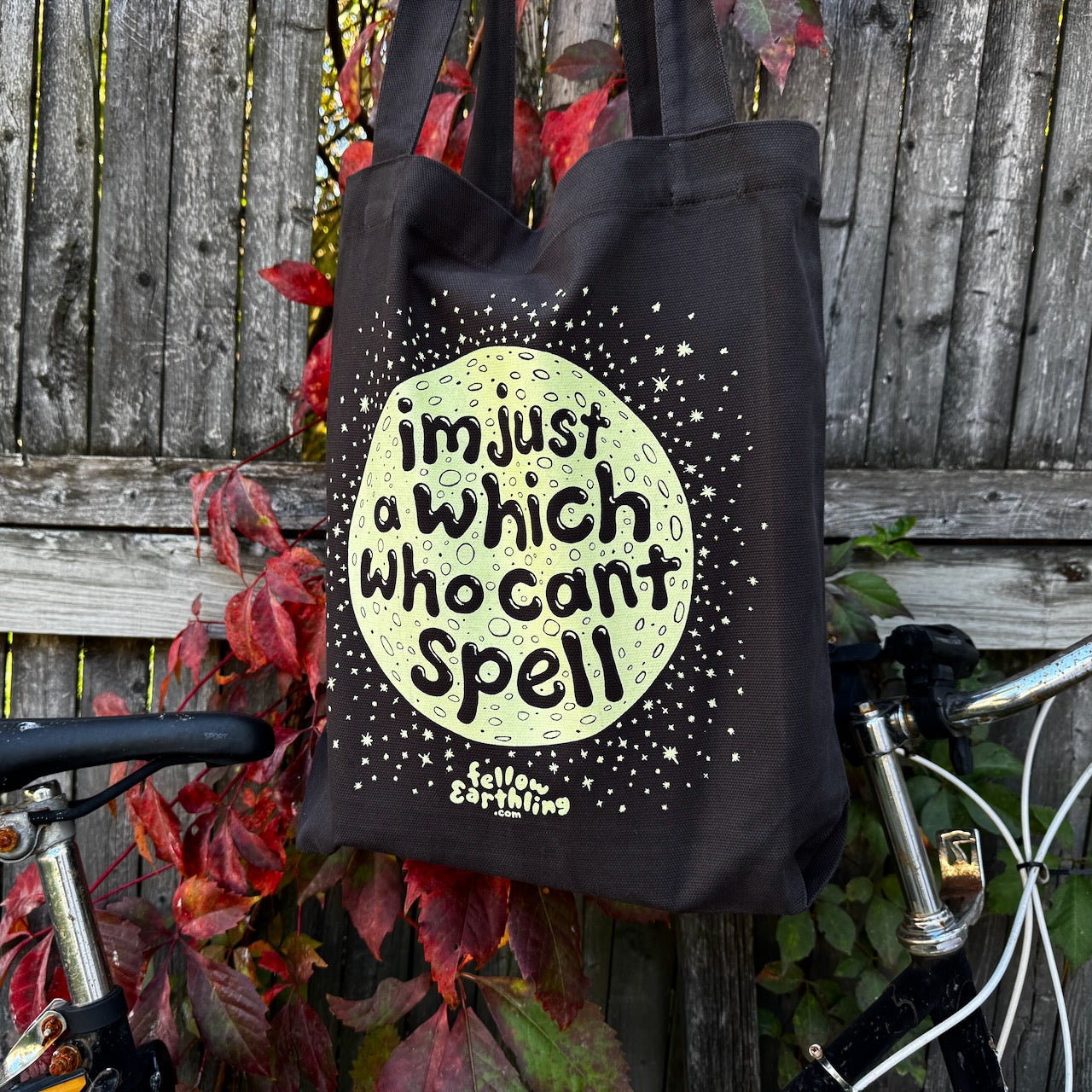 A black tote bag with a moon design that says "I'm just a which who can't spell"