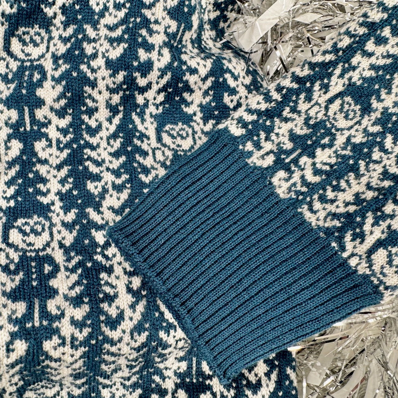 A close up of the knit pattern of a sweater with trees and elves repeating across the garment.