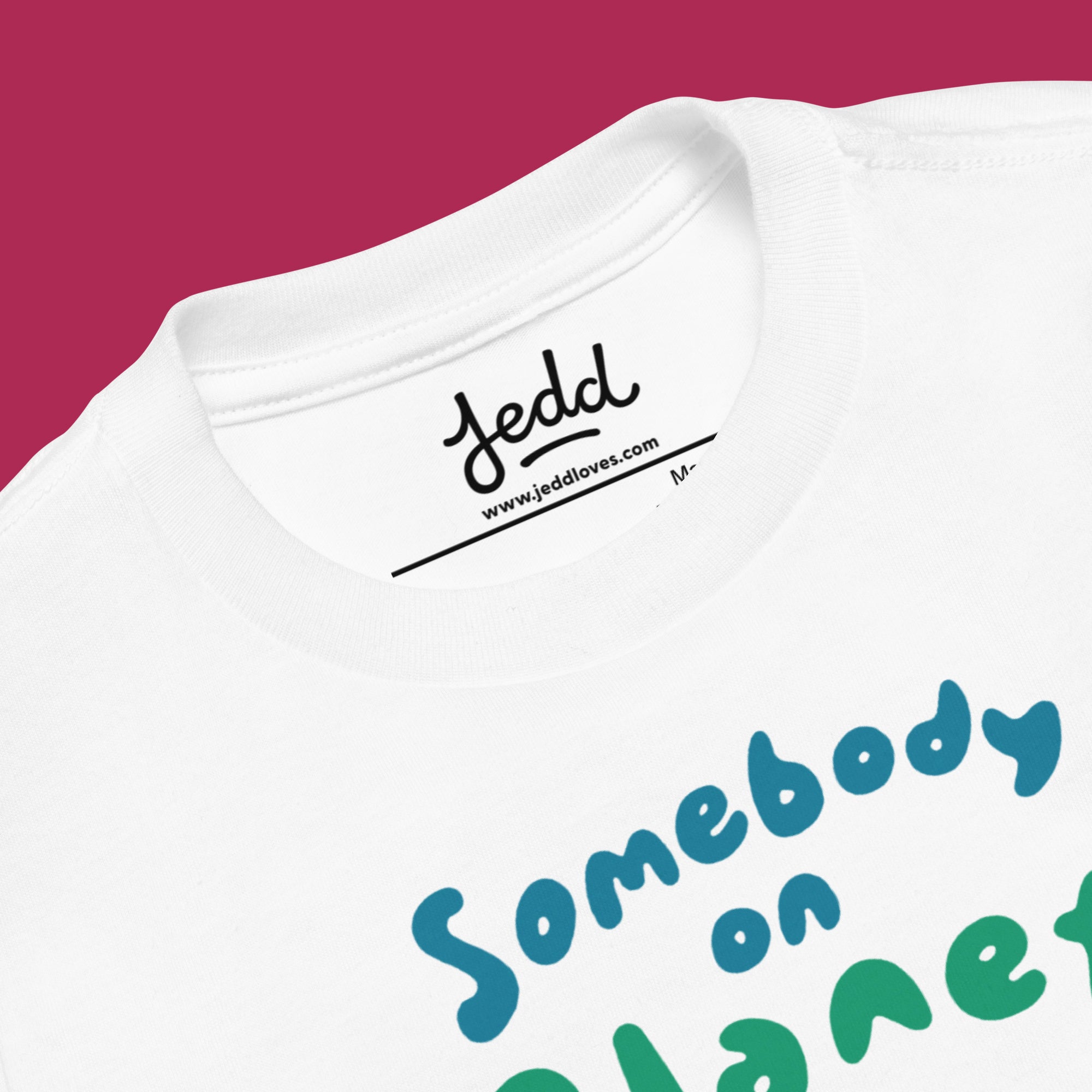 White t-shirt with colorful text 'Somebody on Planet Earth Loves Me' on a magenta background