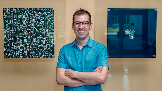 A photo of Jedd standing in front of artwork.