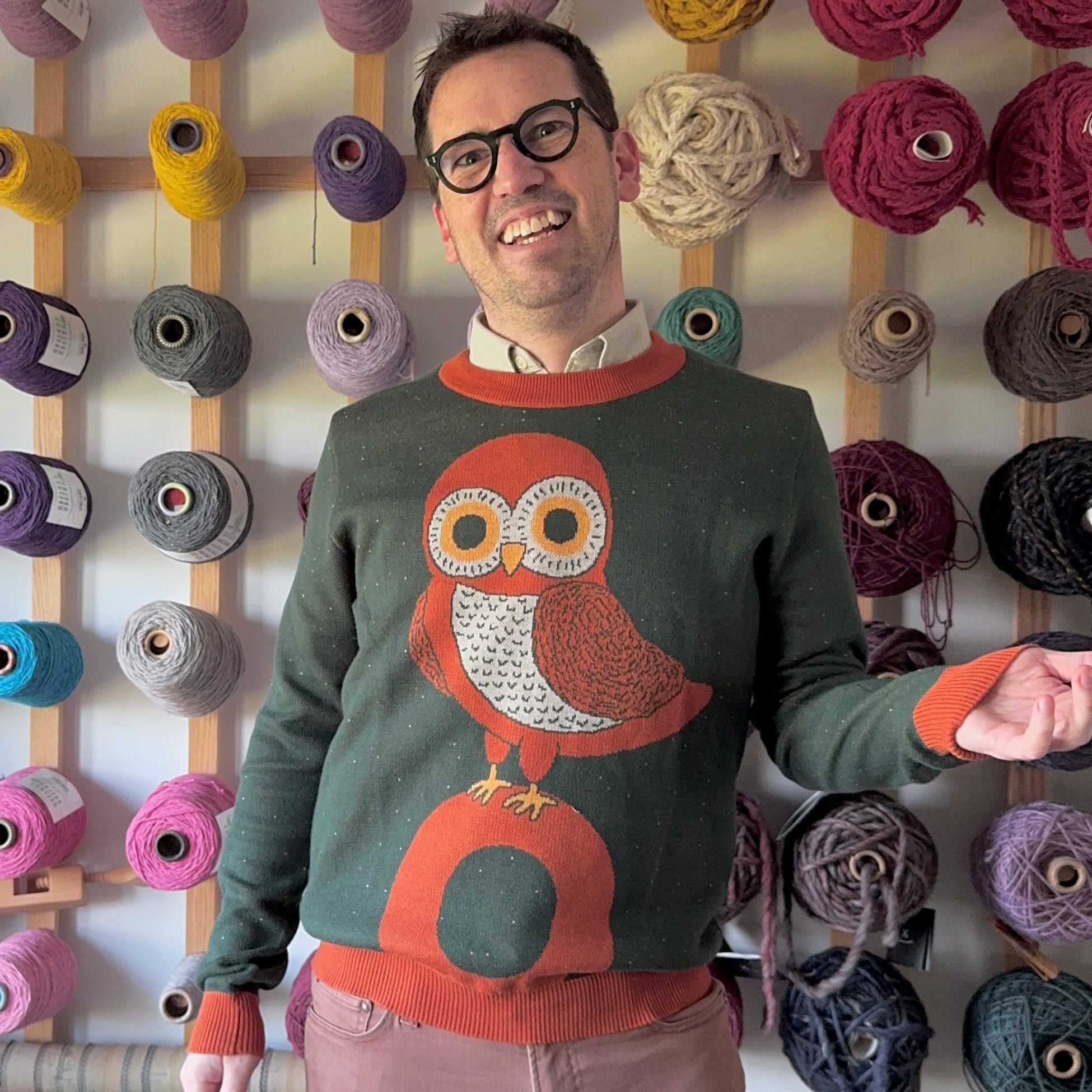 Portrait of Jedd wearing a green sweater with an orange owl illustration.