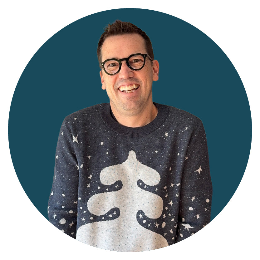 Jedd wearing a navy sweater with a white tree design on a teal background