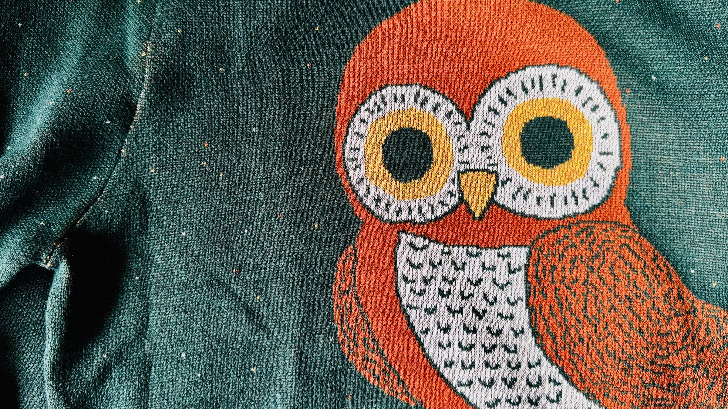 Close-up of a green fabric with an embroidered orange owl design.
