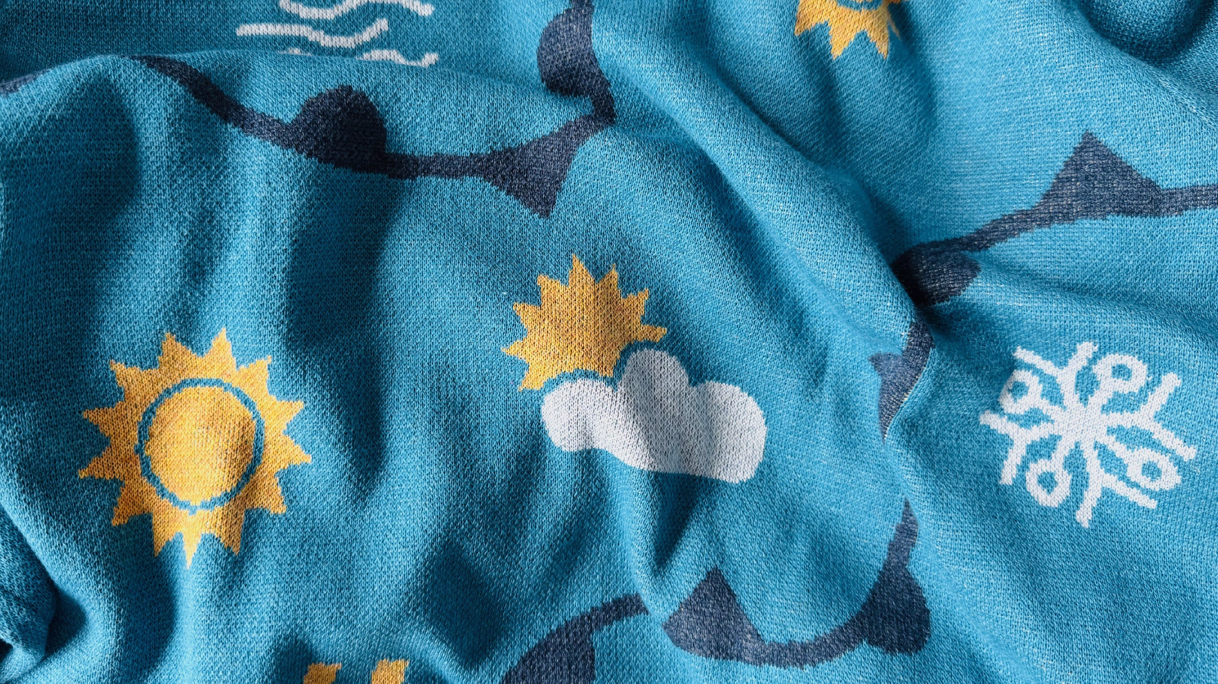 Close-up of a blue fabric with sun, cloud, and wave patterns.