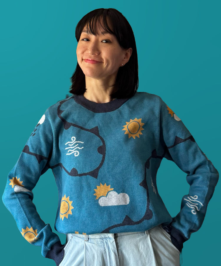 Woman wearing a blue sweater with sun and cloud patterns against a teal background