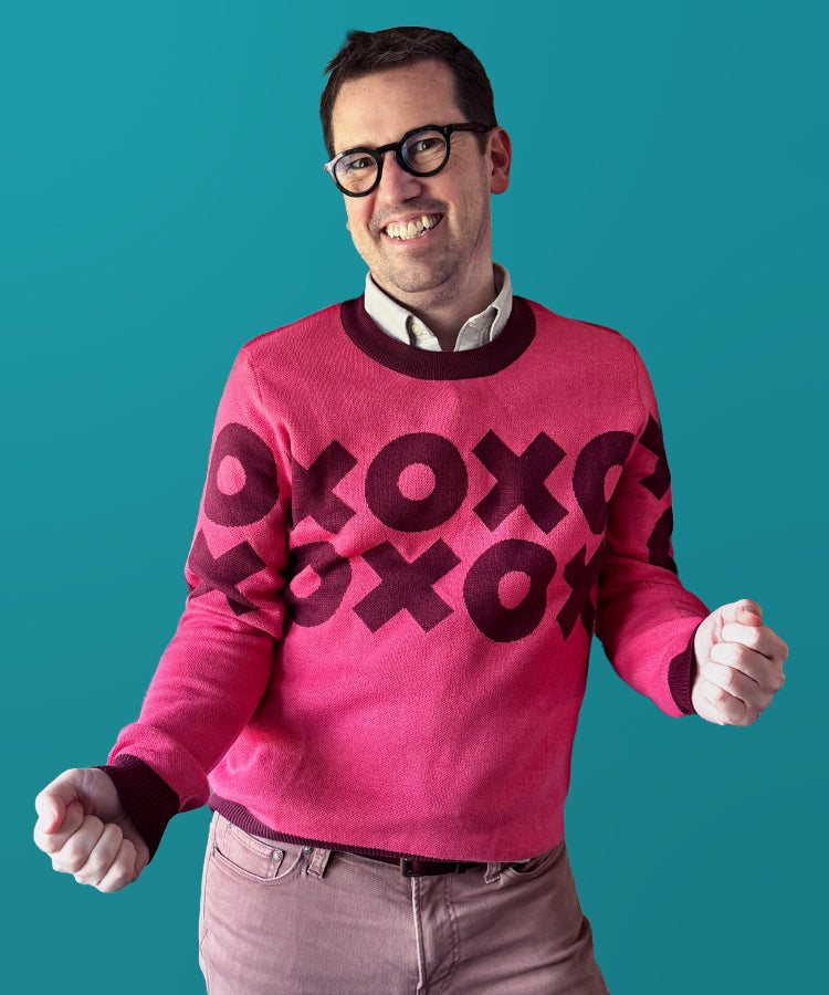 Person wearing a pink sweater with black patterns on a teal background